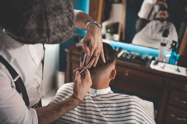 Professional hairdresser doing haircut with scissors in barbershop