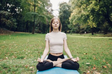 Kız nilüfer çiçeğiyle meditasyon yapıyor. Şehir parkında çimlerde poz veriyor.