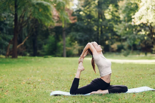 Girl doing yoga in the park on the mat. Yoga exercise outdoor.