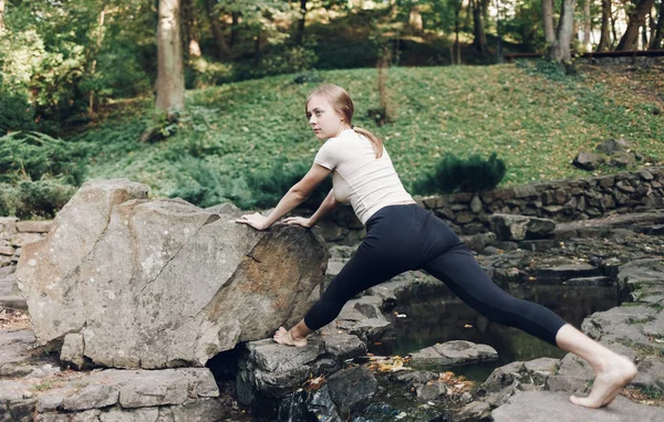Young yoga girl in black leggings doing stretching on the stones