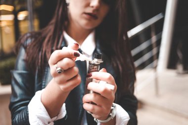 Woman refills liquid in e-cigarette closeup. Girl refills liquid in vape. Electronic cigarette concept