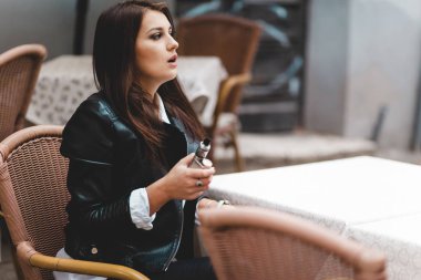 Pretty lady holding electronic cigarette in her hand while sitting at a cafe table