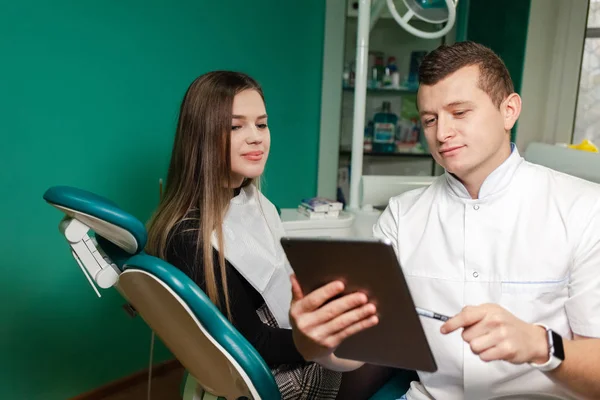 Dentist with tablet shows patient information about upcoming treatment. Modern technologies in stomatology. Modern dentist concept