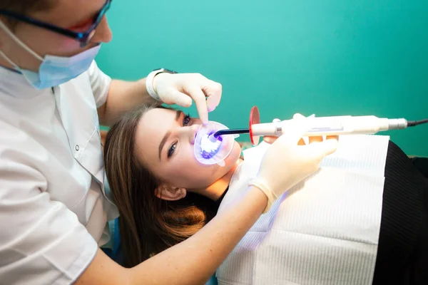 Dentist using whitening ultraviolet lamp on patient teeth.