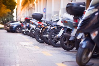 Sokakta park mobiletleri kiralanmış. Otoparkta çok motosiklet var.