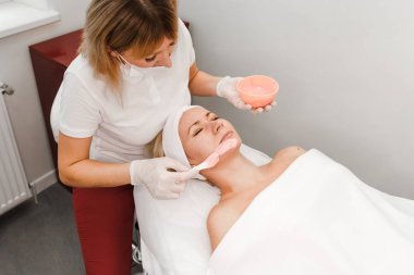 Kozmetik uzmanı müşterinin yüzüne bir maske takıyor.