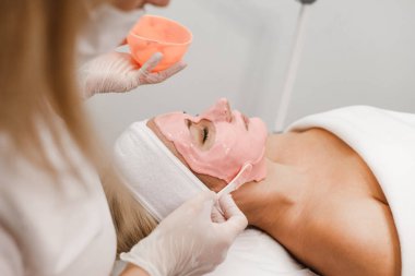 Kozmetik uzmanı müşterinin yüzüne bir maske takıyor.