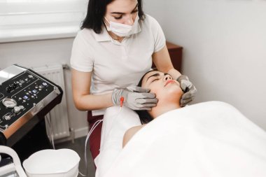 Mikro akım terapisi. Kozmetik uzmanı elektrikli eldivenlerle yüz masajı yapıyor. Lenfatik drenaj masajı