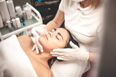 Kozmetik uzmanı müşterinin yüzüne masaj yapıyor.