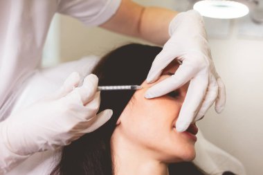 Kozmetik uzmanı hastasına yaşlanma önleyici iğneler yapıyor. Kadın kendine iyi bakıyor ve yüz enjeksiyonlarını yeniliyor.