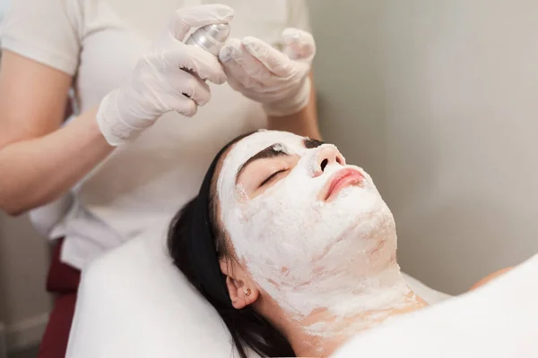 Cosmetologist applies foam on the face of a girl