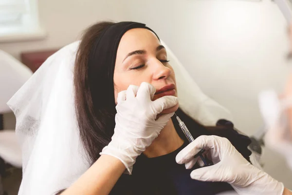 Kadın yüz kırışıklıklarıyla savaşıyor. Doktor kozmetolog hastaya çene iğnesi yapıyor.
