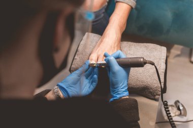 Pedikür ustası pedikür için tırnakları hazırlamak için tırnak törpüsü matkabı kullanır