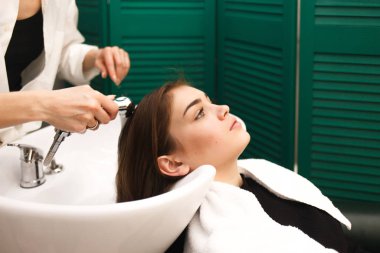 Güzel bir genç kız bir güzellik stüdyosunda kafasını yıkıyor. Kuaför müşteri için saç yıkıyor.