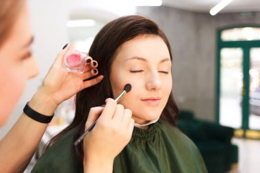 Makyaj sanatçısı makyaj fırçasıyla müşterinin cildine pudra sürüyor. Güzellik salonunda makyaj süreci