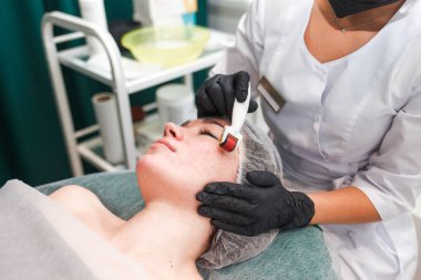 Doctor cosmetologist makes facial massage procedure using a dermo roller. Woman in beauty salon during mesotherapy procedure with mesoscooter clipart