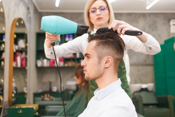 Hairdresser dries hair of stylish man. Young handsome guy doing hair styling at a hairdresser