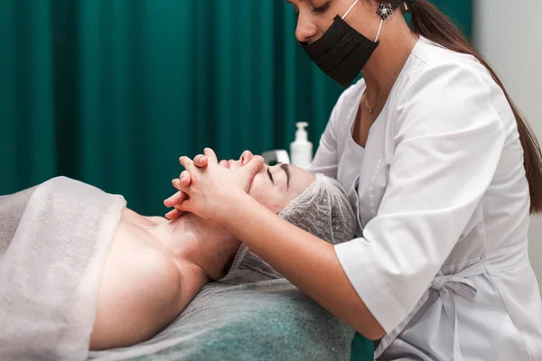 Doctor beautician makes cosmetic facial massage. Woman relaxes on a cosmetic chair side view