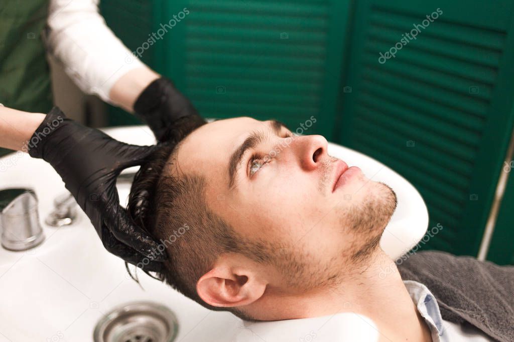 Hairdresser washes a clients hair before cutting. Serious handsome man washes his head in a beauty salon