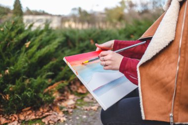 Bir bankta oturan ressamın yan görüntüsü ve bir resim çizer.