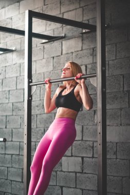 Kaslı kadın yatay çubuğa yanaşıyor. Spor salonundaki yatay barda formda kız eğitimi.