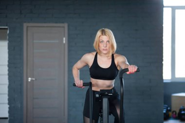 Female uses exercise bike. Woman burns calories on velosimulator. Girl in bicycle training