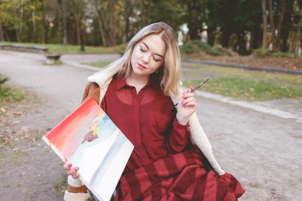 Young girl draws a picture on a park bench. Blonde artist engaged in her favorite hobby of drawing