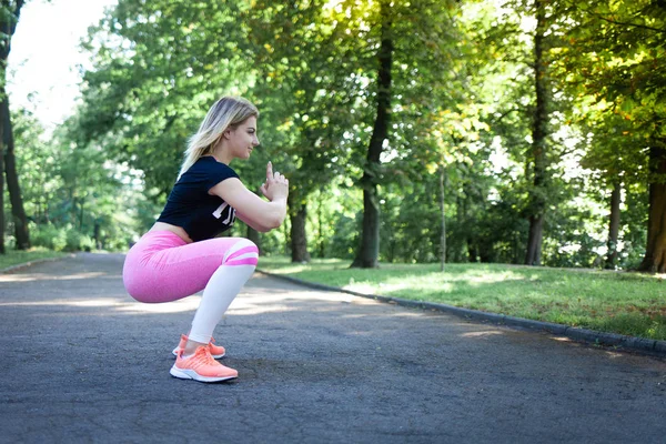 Attractive girl in pink leggings does squats. Athletic fitness lady doing buttock exercises — ストック写真