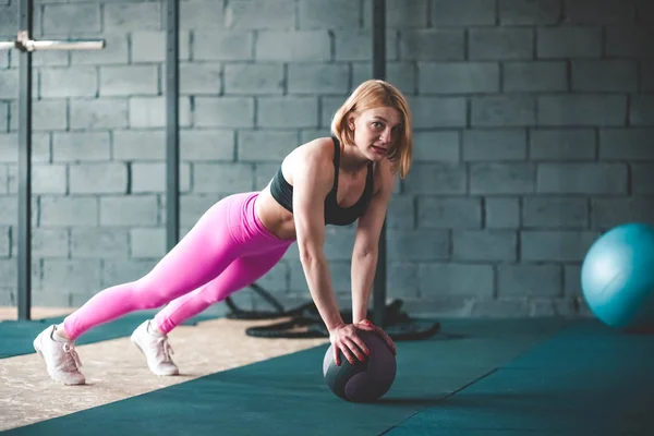 Girl doing exercise with a medical ball. Fitness lady with medicine ball training in gym