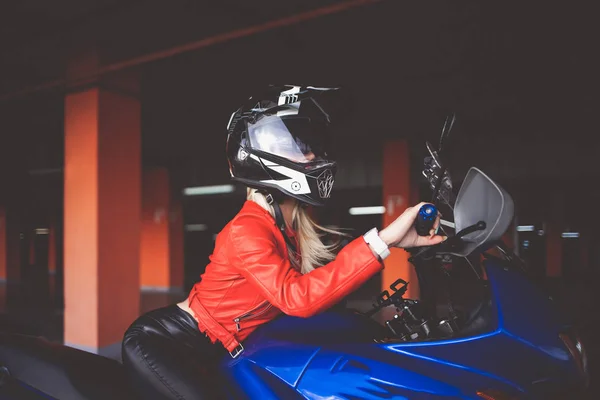 戴着头盔的年轻自行车手在一辆跑车上摆姿势 在地下停车场骑摩托车的女孩 — 图库照片