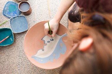 Potter denen kadın seramik tabak boyuyor. Kız toprak eşyalar üzerinde bir fırçayla resim çiziyor. Kil ürünleri oluşturma süreci.