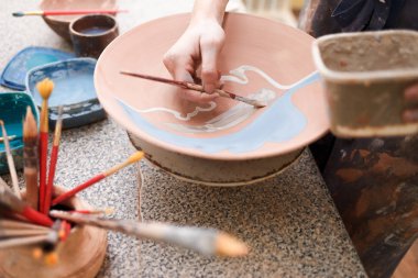 Potter denen kadın seramik tabak boyuyor. Kız toprak eşyalar üzerinde bir fırçayla resim çiziyor. Kil ürünleri oluşturma süreci