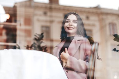 Pozitif genç esmer kız kafede oturuyor ve pencereden dışarı bakıyor.