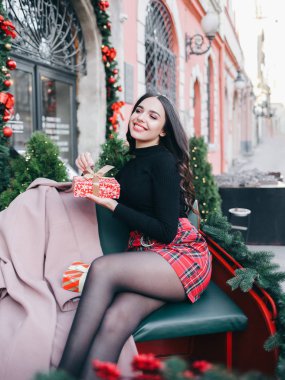 Güzel bayan yeni yıl hediyesine çok sevindi. Güzel genç kız kutusunu bir yılbaşı hediyesiyle açıyor. Elinde bir hediye olan kadın, Noel süslerinin arkasında duruyor.