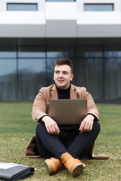 Student working on a laptop outdoor. Man sits with a laptop in his hands on the backcground of a business center