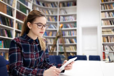Kütüphanede tabletle çalışan bir kız. Öğrenci kitaplardan çok bir tabletle çalışmayı tercih eder.