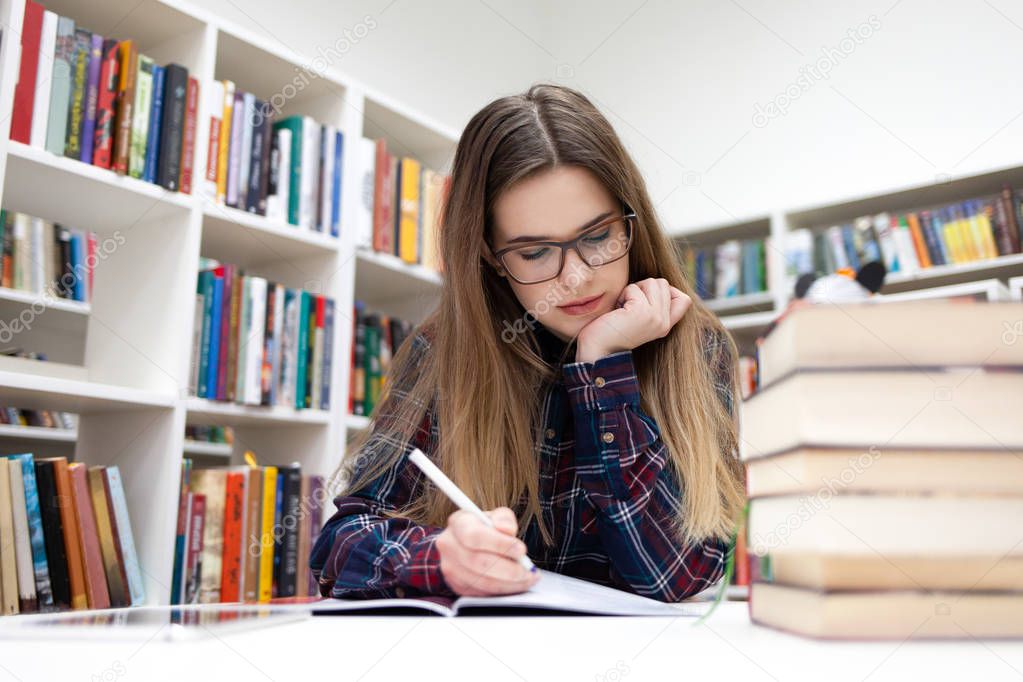 Girls writes in the library. Young student studying at the campus library