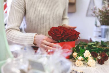 Çiçekçi kadın kırmızı güllerle kutu yapıyor. Çiçekli şapka kutusu oluşturma süreci