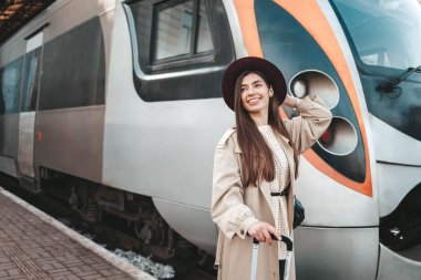 Güzel gezgin, tren istasyonunda arka planda dururken elini sallıyor.