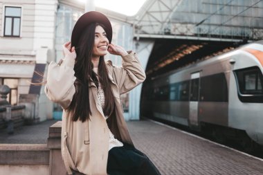 Tren istasyonunda şapkalı, gülen kız tren kalkışını bekliyor.