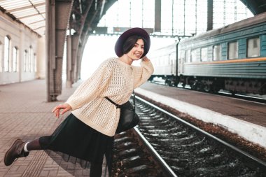 Tren istasyonunda şapkalı, gülen kız tren kalkışını bekliyor.