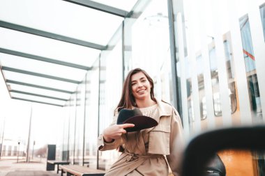 Girl in stylish clothes sits at a bus stop and is about to throw her hat up