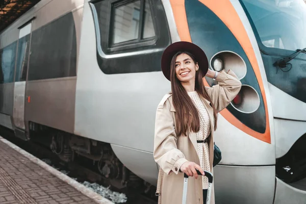 Güzel gezgin, tren istasyonunda arka planda dururken elini sallıyor.