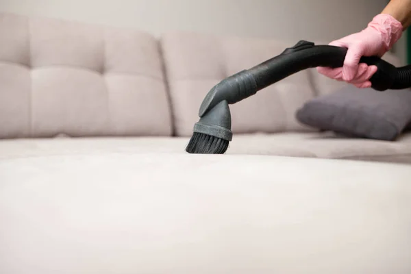 close up of woman\'s hand cleaning couch using vacuum cleaner at home sofa