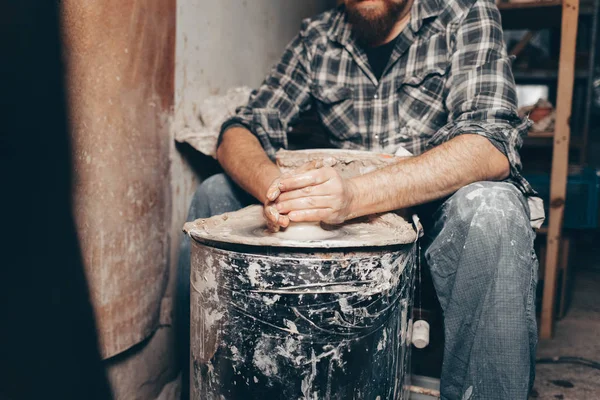 Man forms a white clay product on a pottery wheel