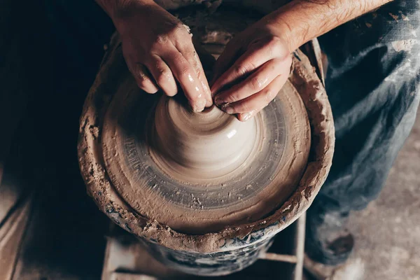 Man forms a white clay product on a pottery wheel top view