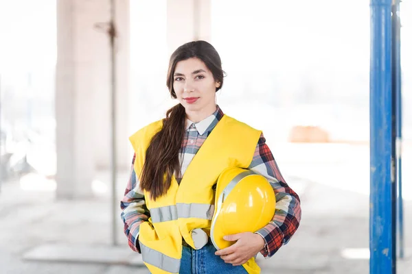 Female engineer stands at a construction site and holding a hardhat in hand