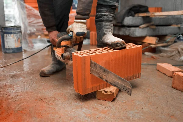 Construction worker cuts a brick with a saw
