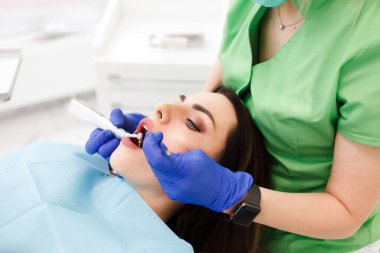 Genç ve güzel bir kadın dişçi dolabında dişlerini tedavi ediyor. Diş tedavisi süreci