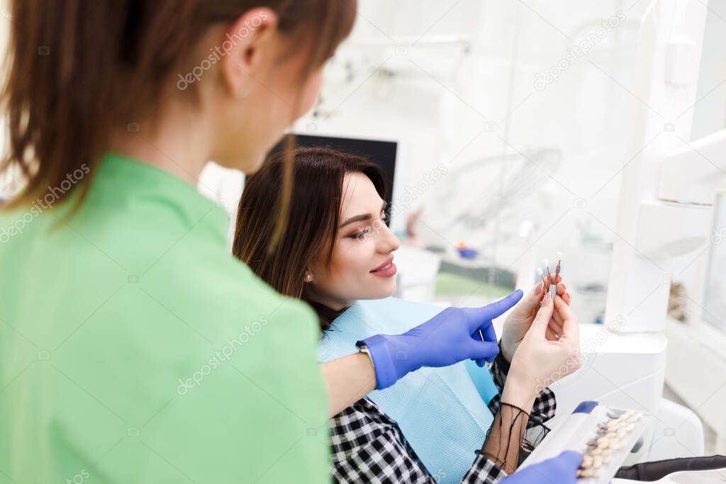 Dentist shows crown samples to his patient. Woman at the dentist's appointment chooses the tone of veneers